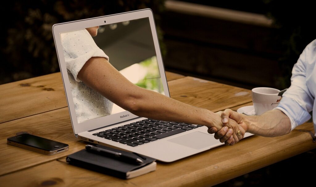 O braço passa pela tela do laptop para apertar a mão
