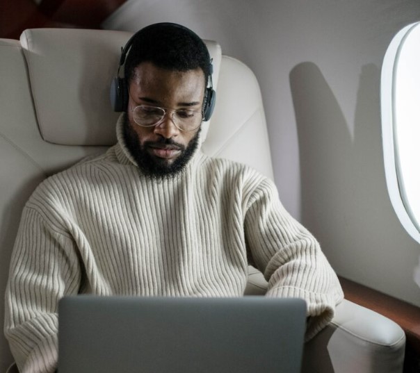 수염과 안경을 쓴 남성이 비행기에서 노트북을 열고 있습니다.