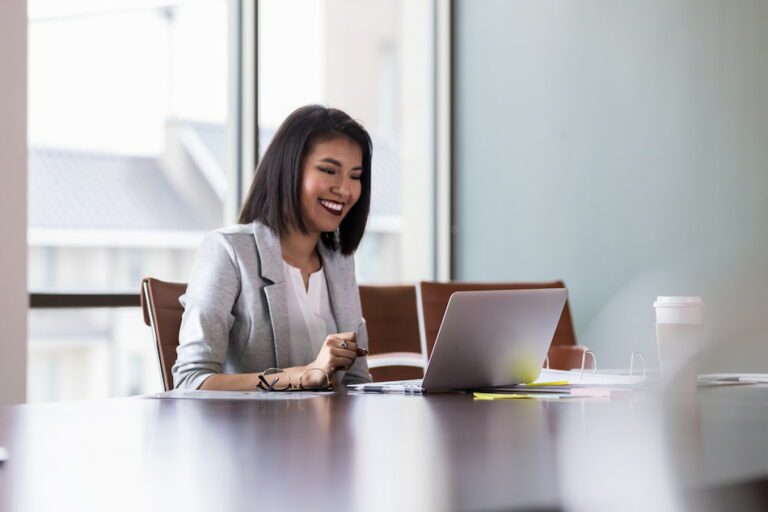 Une femme sourit devant un ordinateur portable dans un bureau.