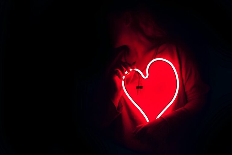 pessoa segurando uma placa de coração de neon no escuro
